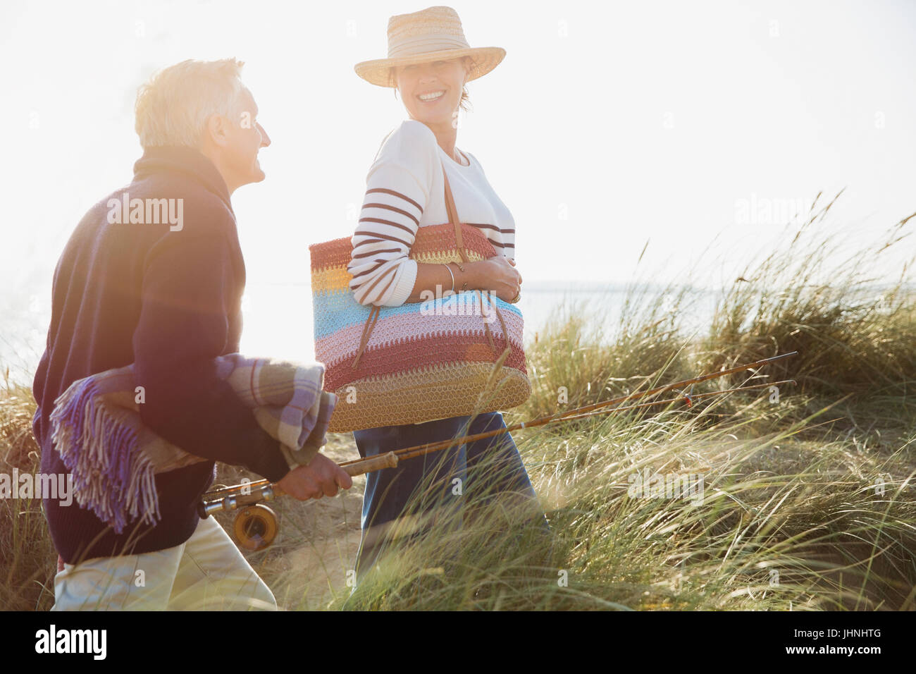 Älteres paar lächelnd mit Angelrute Wandern im sonnigen Strandhafer Stockfoto