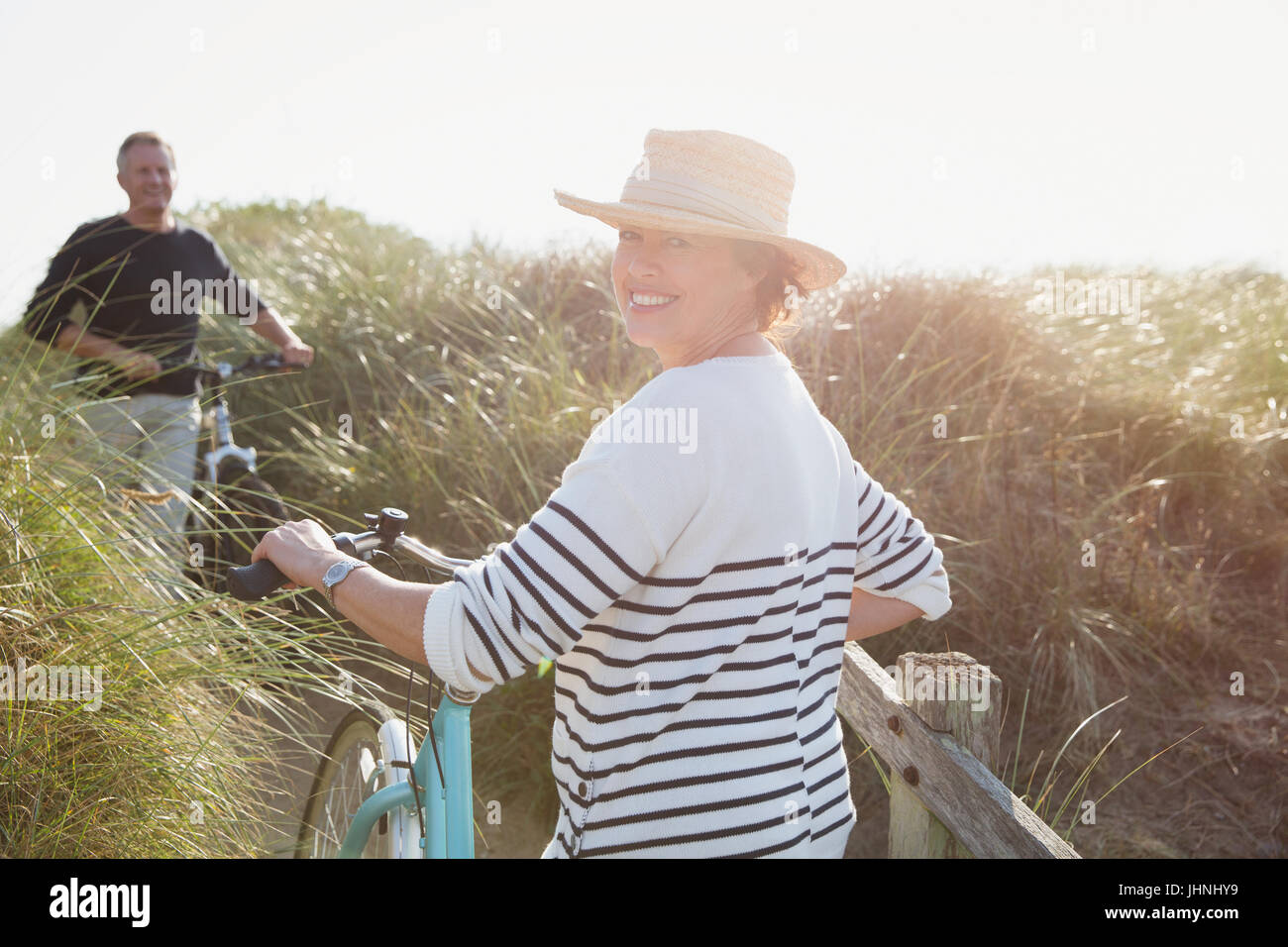 Porträt lächelnd Reife Frau Fahrrad auf sonnigen Strandhafer Weg gehen Stockfoto
