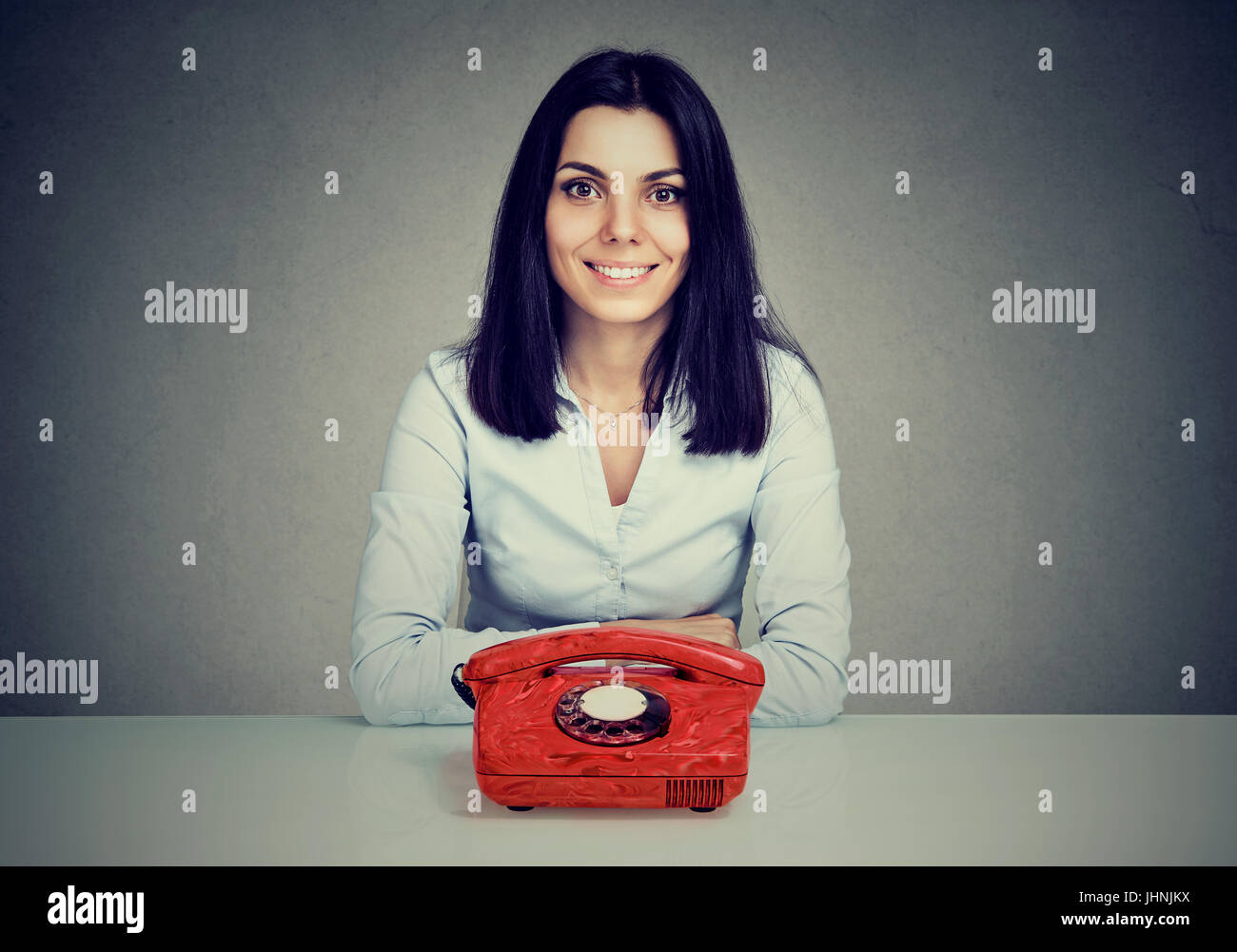 Glückliche Frau sitzt am Tisch mit Vintage rotes Telefon Stockfoto