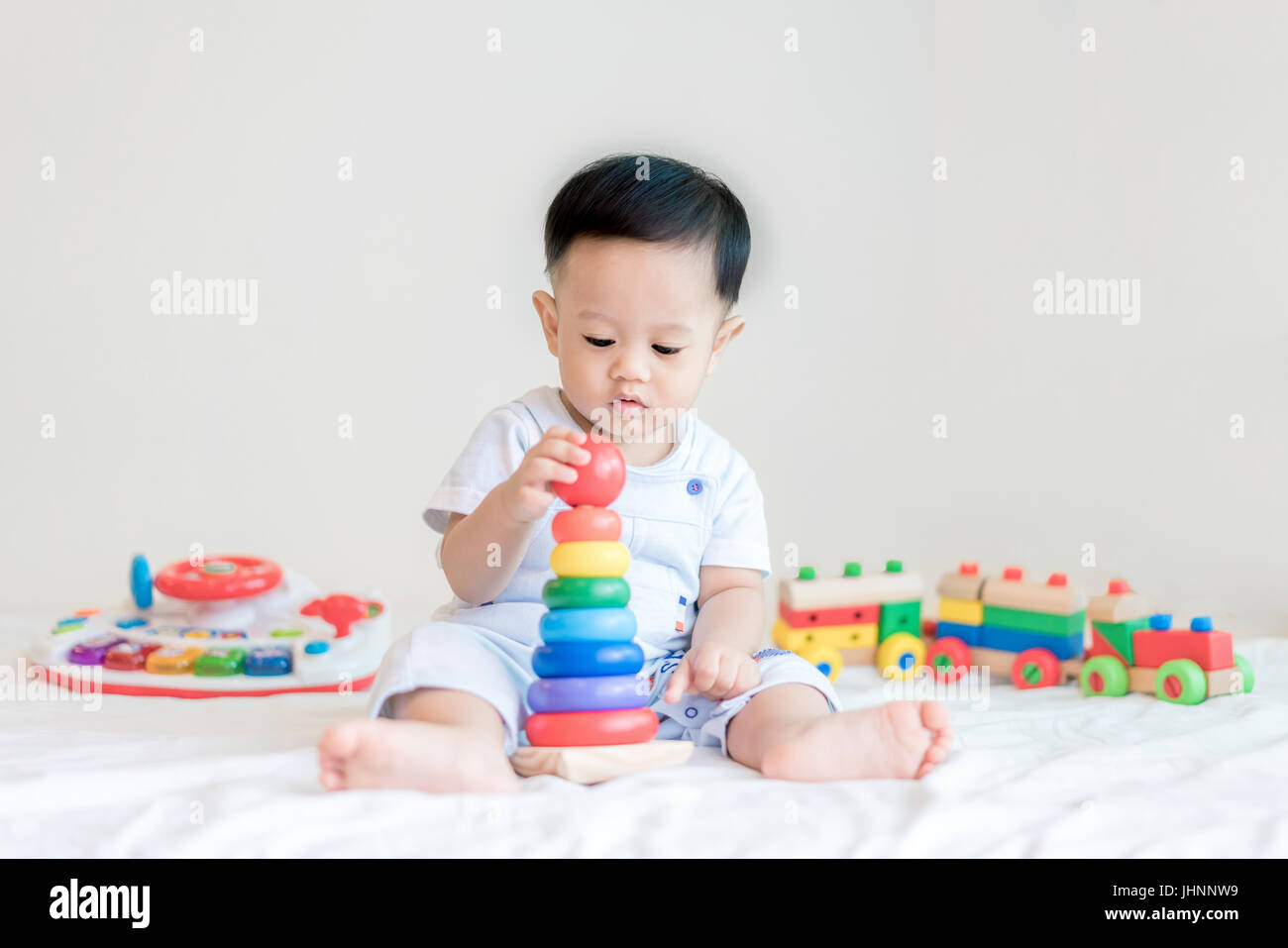 Entzückende asiatische Baby junge 9 Monate am Bett sitzen und spielen mit Farbe Entwicklungsstörungen Spielzeug zu Hause. Stockfoto