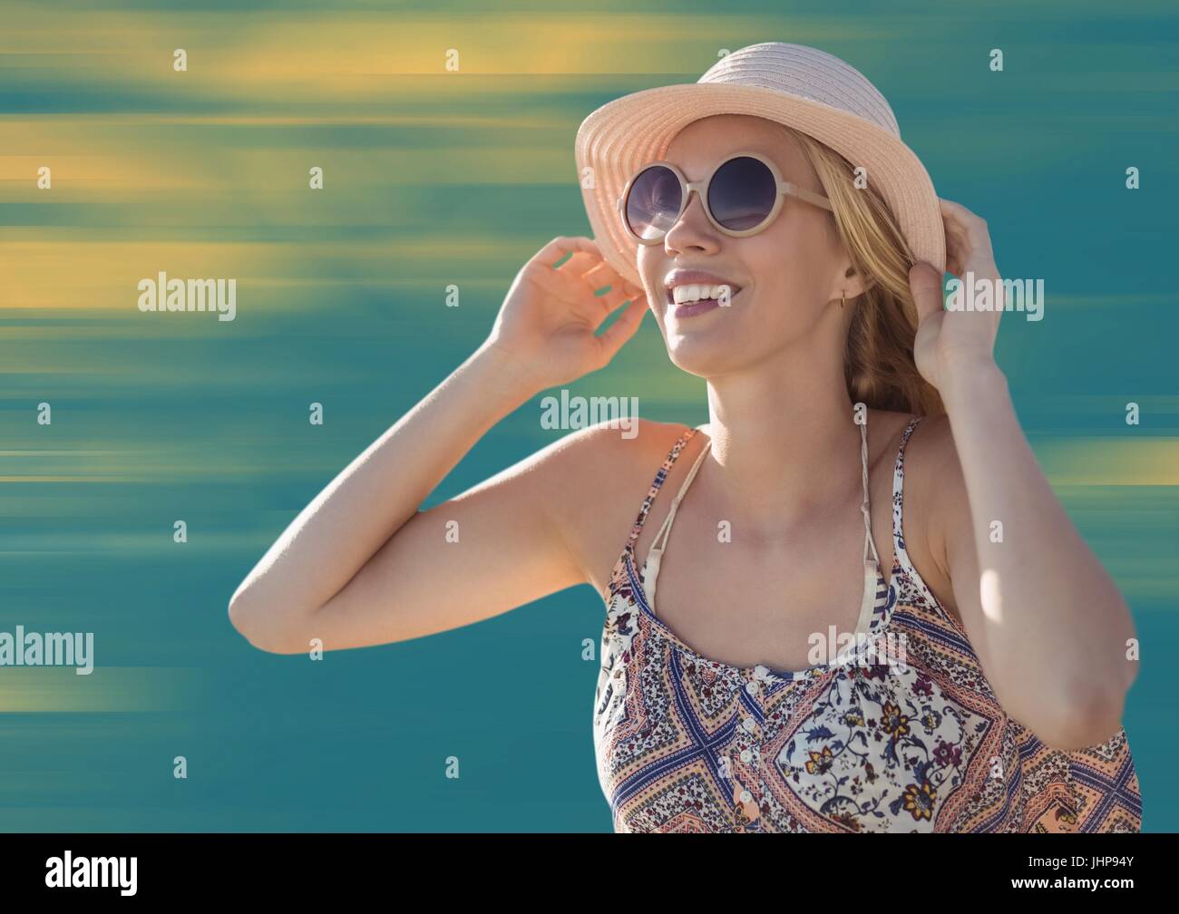 Digital Composite Frau mit Hut und Sonnenbrille vor verschwommen gelben und blauen Hintergrund Stockfoto