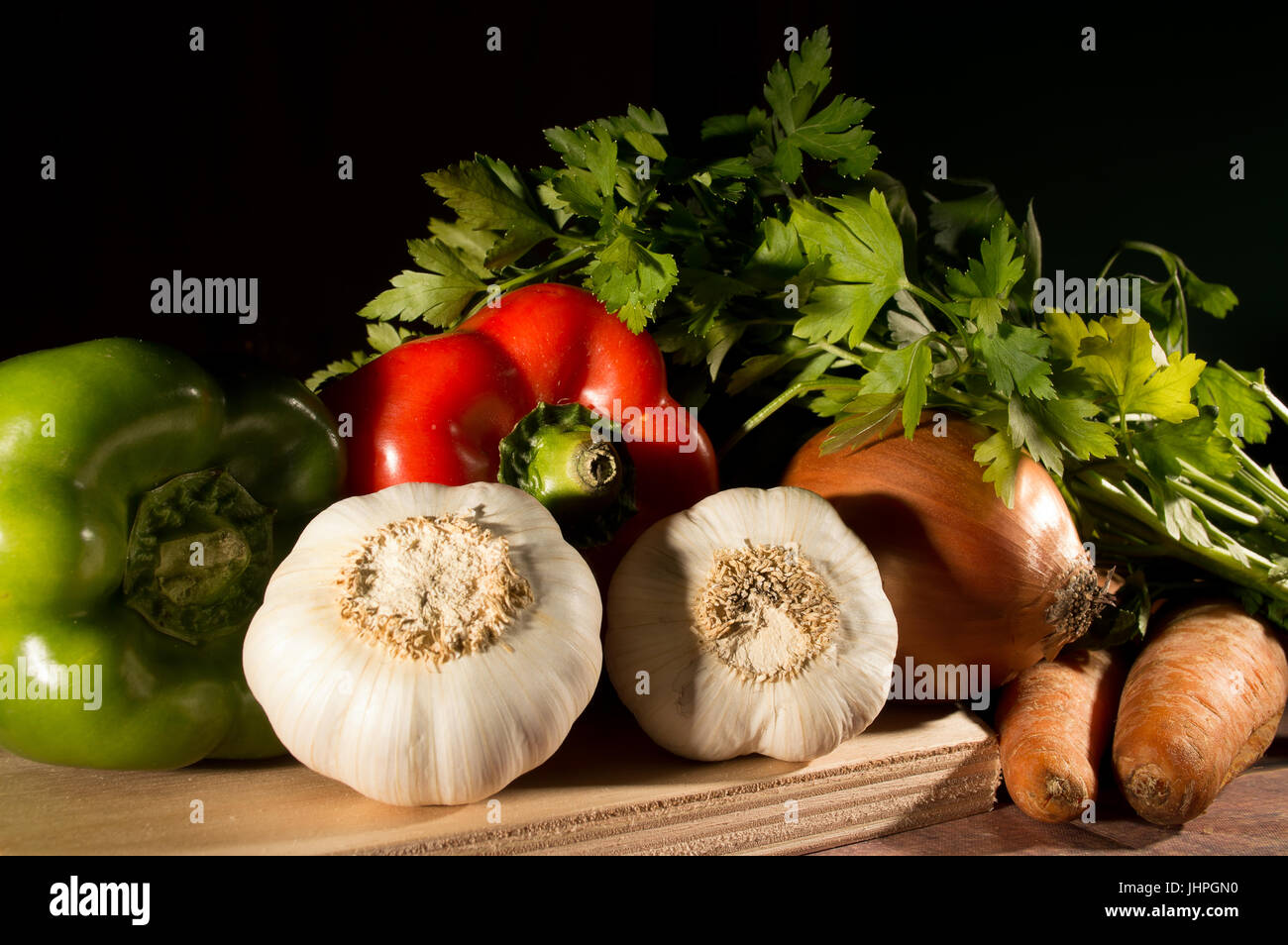 Knoblauch, Paprika, Zwiebel, Möhren und Petersilie gruppierte und bereit zum Garen auf schwarzem Hintergrund Stockfoto