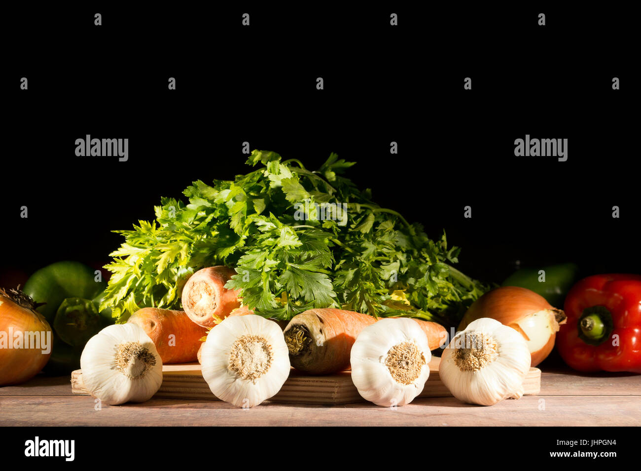 Knoblauch, Karotten, Zwiebeln, Paprika und Petersilie gruppiert auf Holztisch auf schwarzem Hintergrund Stockfoto