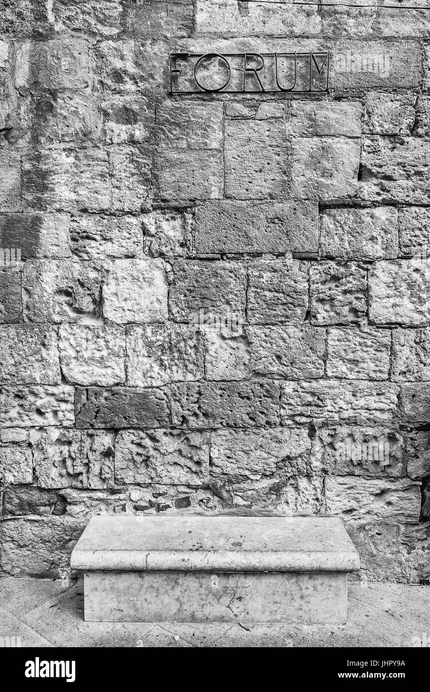 Stein-Sitzbank mit einer Mauer aus Steinen in den Hintergrund, und das Wort Forum darüber Stockfoto