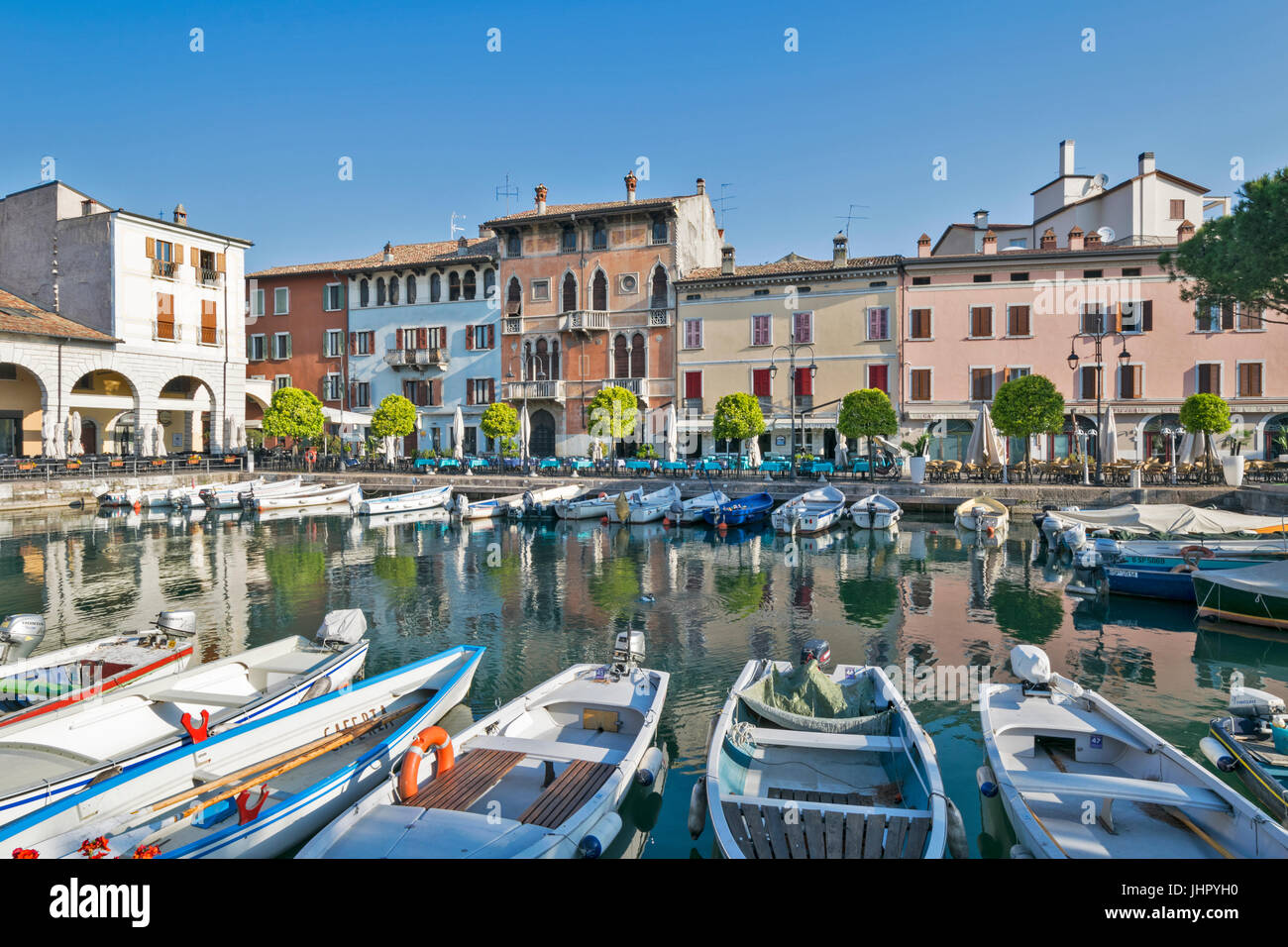 Italien GARDASEE DESENZANO DEL GARDA AM FRÜHEN MORGEN DEN HAFEN MIT BOOTEN UND DIE UMLIEGENDEN FARBIGEN HÄUSER UND RESTAURANTS IM APRIL Stockfoto