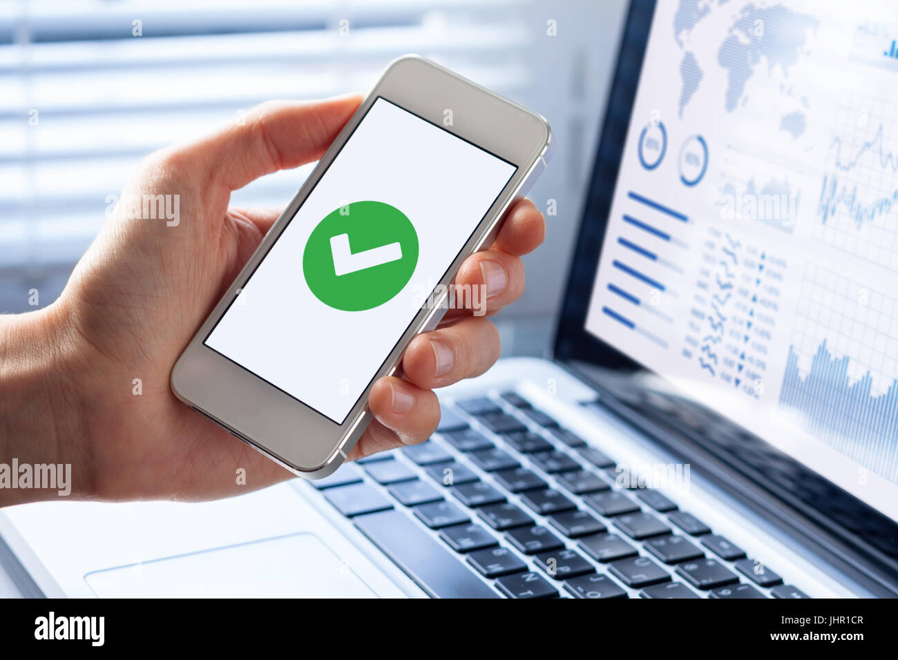 Hand, die ein Smartphone mit einem grünen Häkchen-Symbol auf dem Bildschirm, um eine validierte, bestätigten, zeigen abgeschlossen oder Status genehmigt Stockfoto