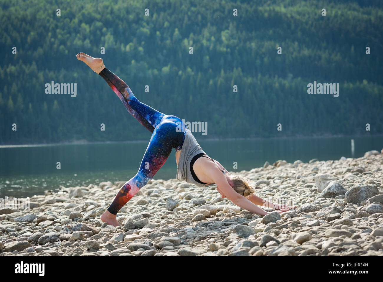 Seitenansicht der Frau praktizieren Yoga am felsigen Ufer gegen Bäume Stockfoto