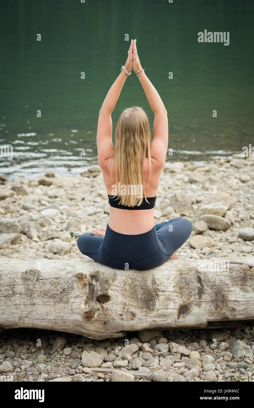 Rückansicht der Frau praktizieren Yoga auf Log am Seeufer Stockfoto
