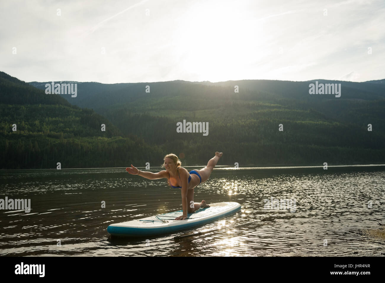 Frau praktizieren Yoga auf Paddleboard im See gegen Himmel Stockfoto