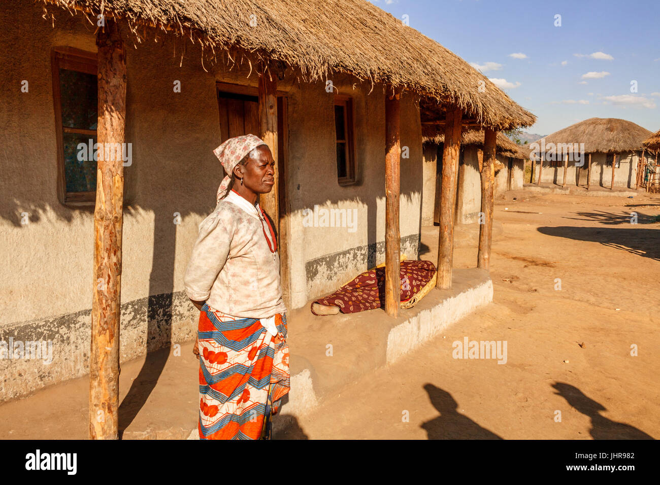 Malawische Frau steht außerhalb ihrer traditionellen Lehmziegeln gebaut Dorfhaus wacht über ihr krankes Kind, die auf der Veranda (Khonde) in einem Blatt liegt. Stockfoto