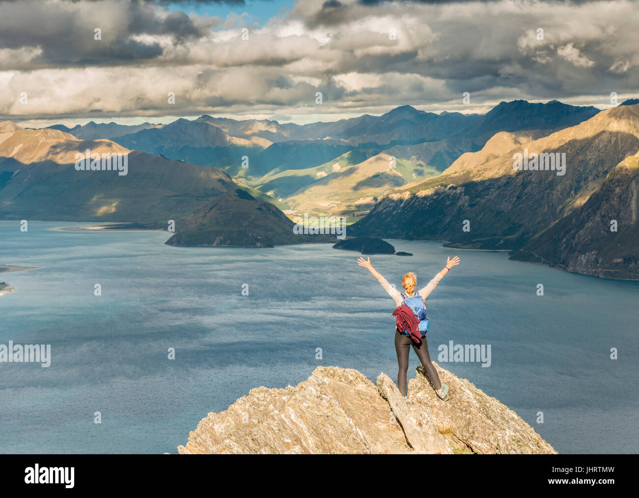 Weibliche Wanderer auf einem Felsen, streckte die Arme in die Luft, Lake Hawea und Berglandschaft, Isthmus Peak, Otago, Südinsel Stockfoto