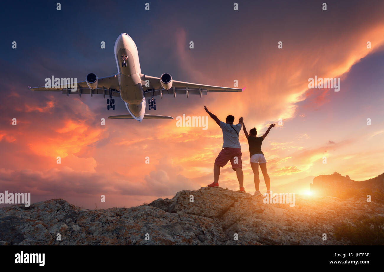 Passagierflugzeug und glückliche Menschen auf dem Berg gegen bunte Himmel bei Sonnenuntergang. Landschaft mit kommerziellen Flugzeug und stehender Mann und Frau mit Stockfoto