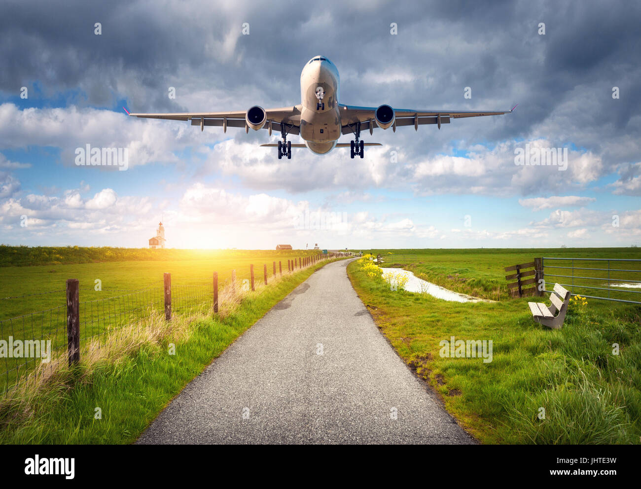 Flugzeug und Landstraße. Landschaft mit Passagierflugzeug fliegt über die Asphaltstraße gegen bewölktem Himmel, grüne Wiese. Reise. Passagier ein Stockfoto