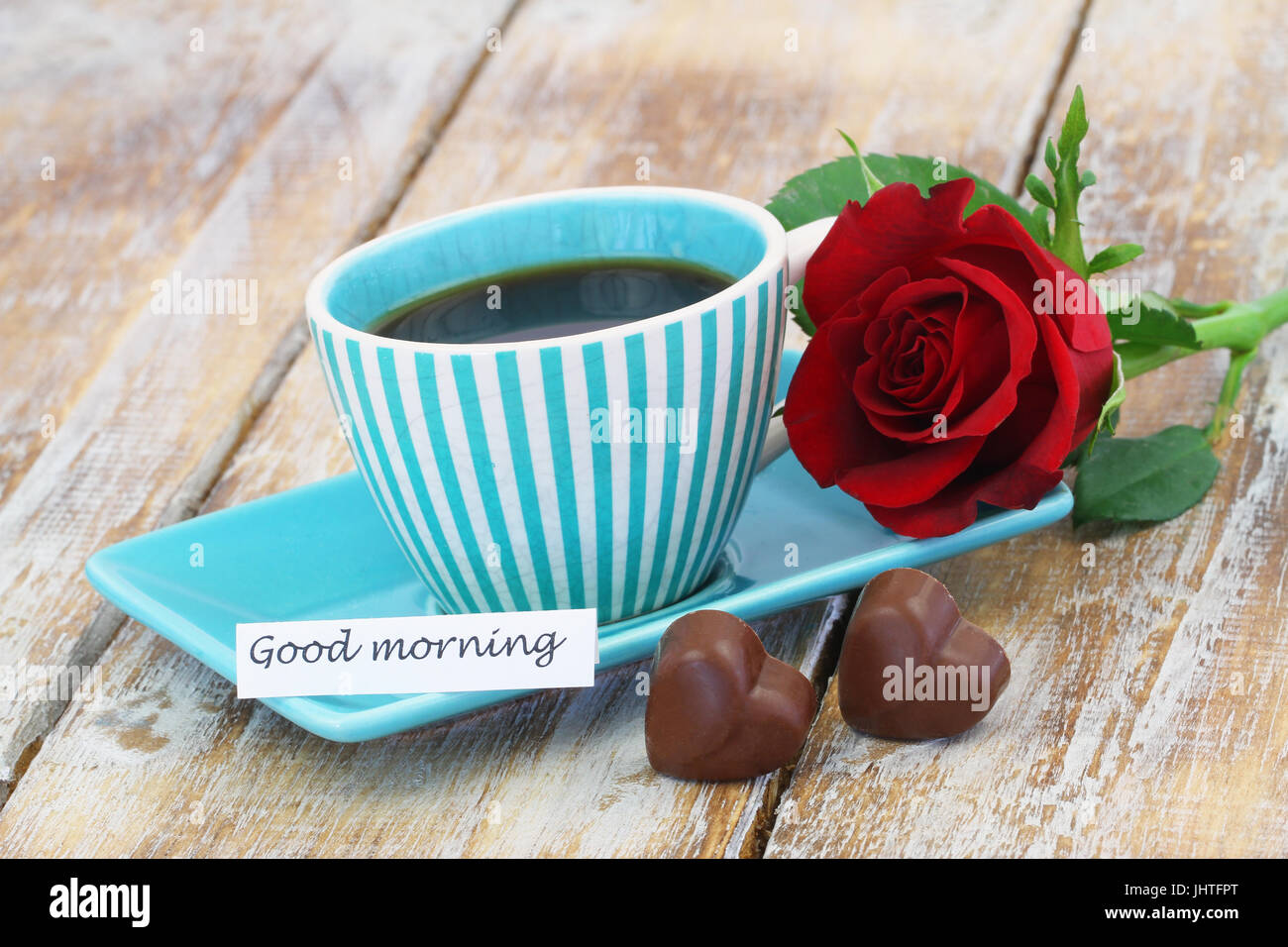 Guten Morgen Karte mit Tasse Kaffee, zwei Herzförmige Pralinen und rote Rose auf rustikalen Holzoberfläche Stockfoto