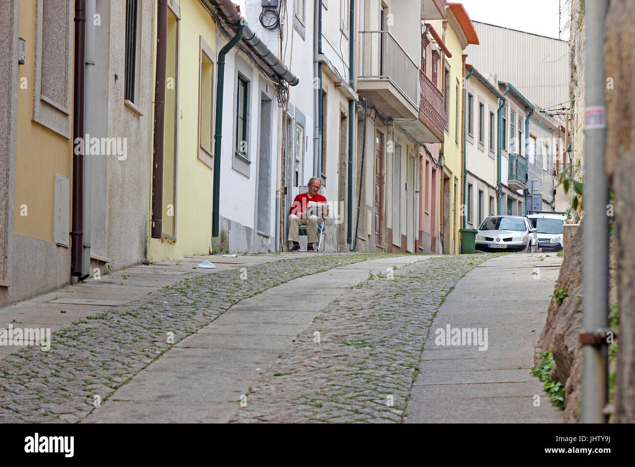 Älterer Mann liest Papier vor seinem Haus auf eine steinerne Gasse Vila Do Conde, Portugal Stockfoto