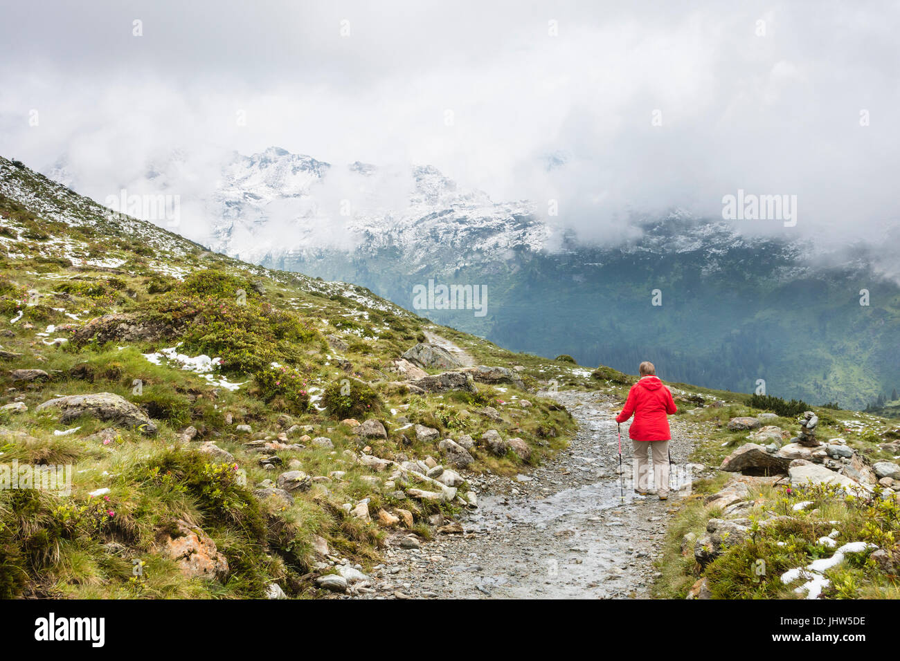 Ein weiblicher senior Wanderer trägt einen roten Mantel, Wandern in das Paznaun-Tal in der Nähe von Galtur in Österreich. Stockfoto