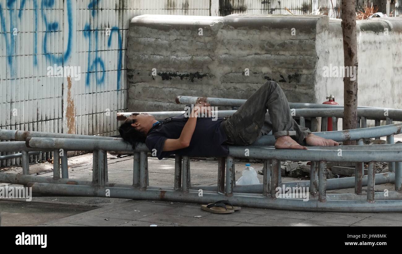 Mann schläft auf einer Sitzbank Stadtpark Freifläche in Sathorn/Saphan Taksin BTS Skytrain-Station Bangkok Thailand Stockfoto