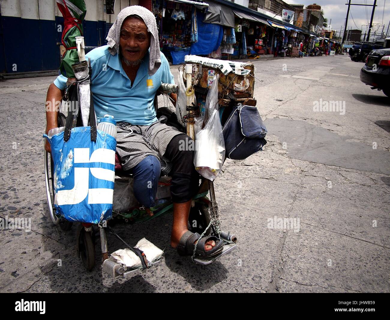 CAINTA CITY, Philippinen - 12. Juli 2017: Ein Alter behinderter Mann rollt in seinem Rollstuhl auf einem öffentlichen Markt. Stockfoto
