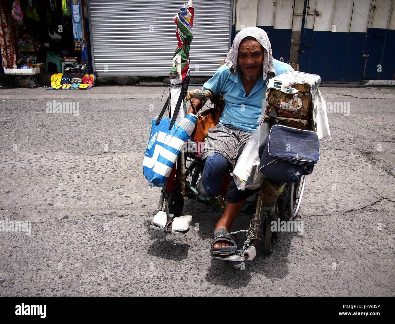CAINTA CITY, Philippinen - 12. Juli 2017: Ein Alter behinderter Mann rollt in seinem Rollstuhl auf einem öffentlichen Markt. Stockfoto