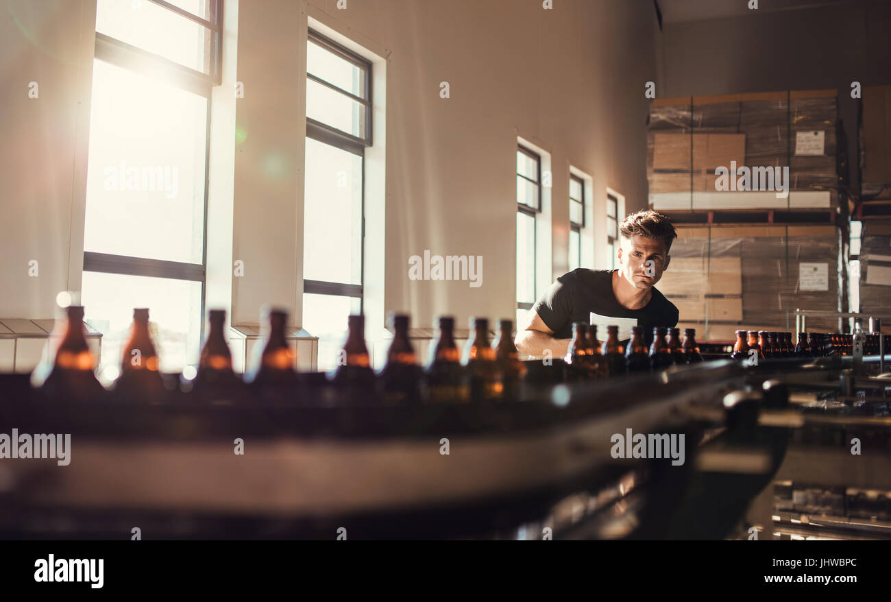 Brewer, Förderband mit Bierflaschen zu betrachten. Junger Mann, Überwachung der Herstellung von Bier im Brauerei-Werk. Stockfoto