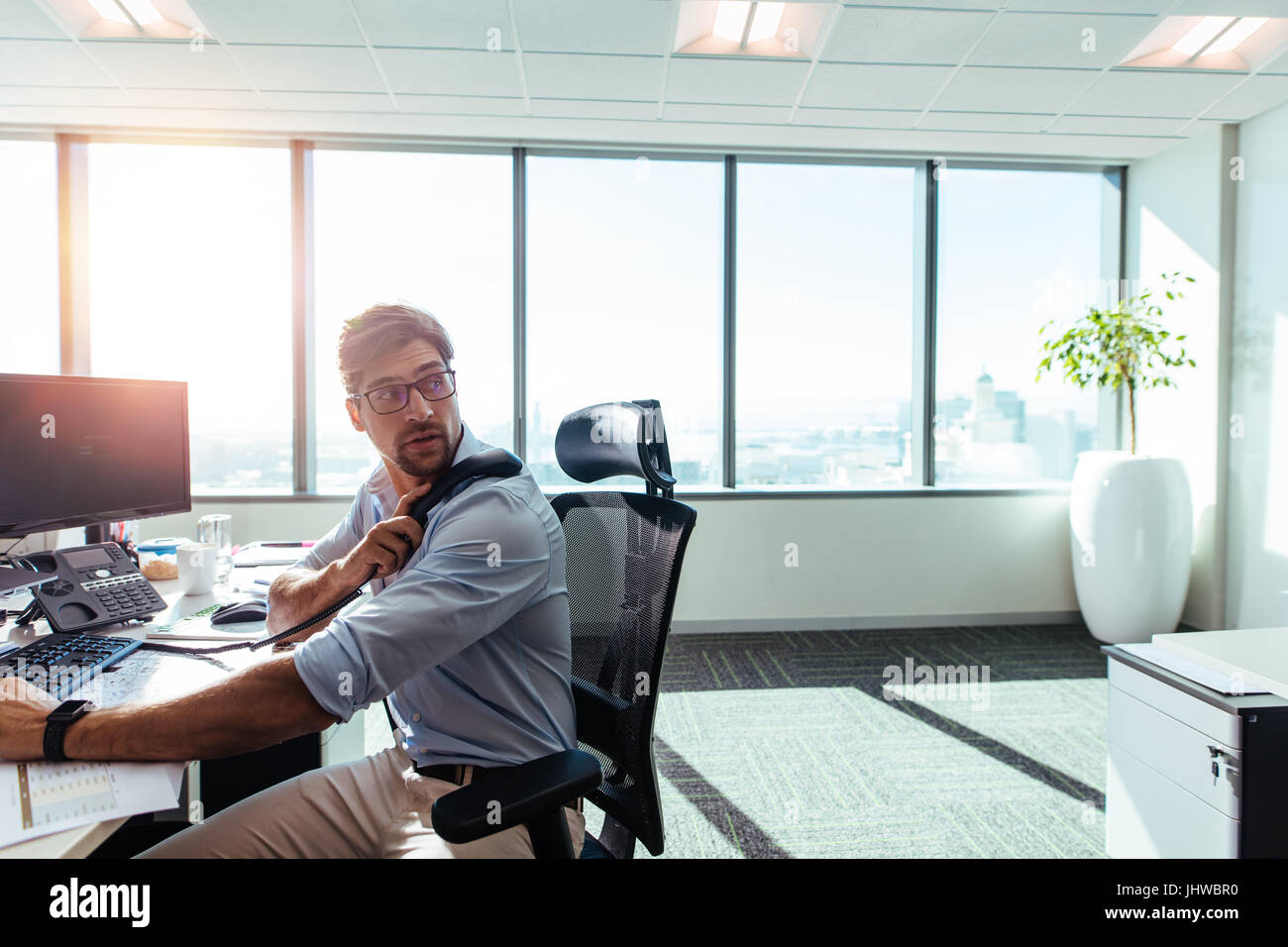 Geschäftsmann in seinem Büro mit Computer und Geschäftspapiere auf Tisch arbeiten. Junge Unternehmer auf der Suche hinter den Empfänger während auf Abruf zu halten Stockfoto