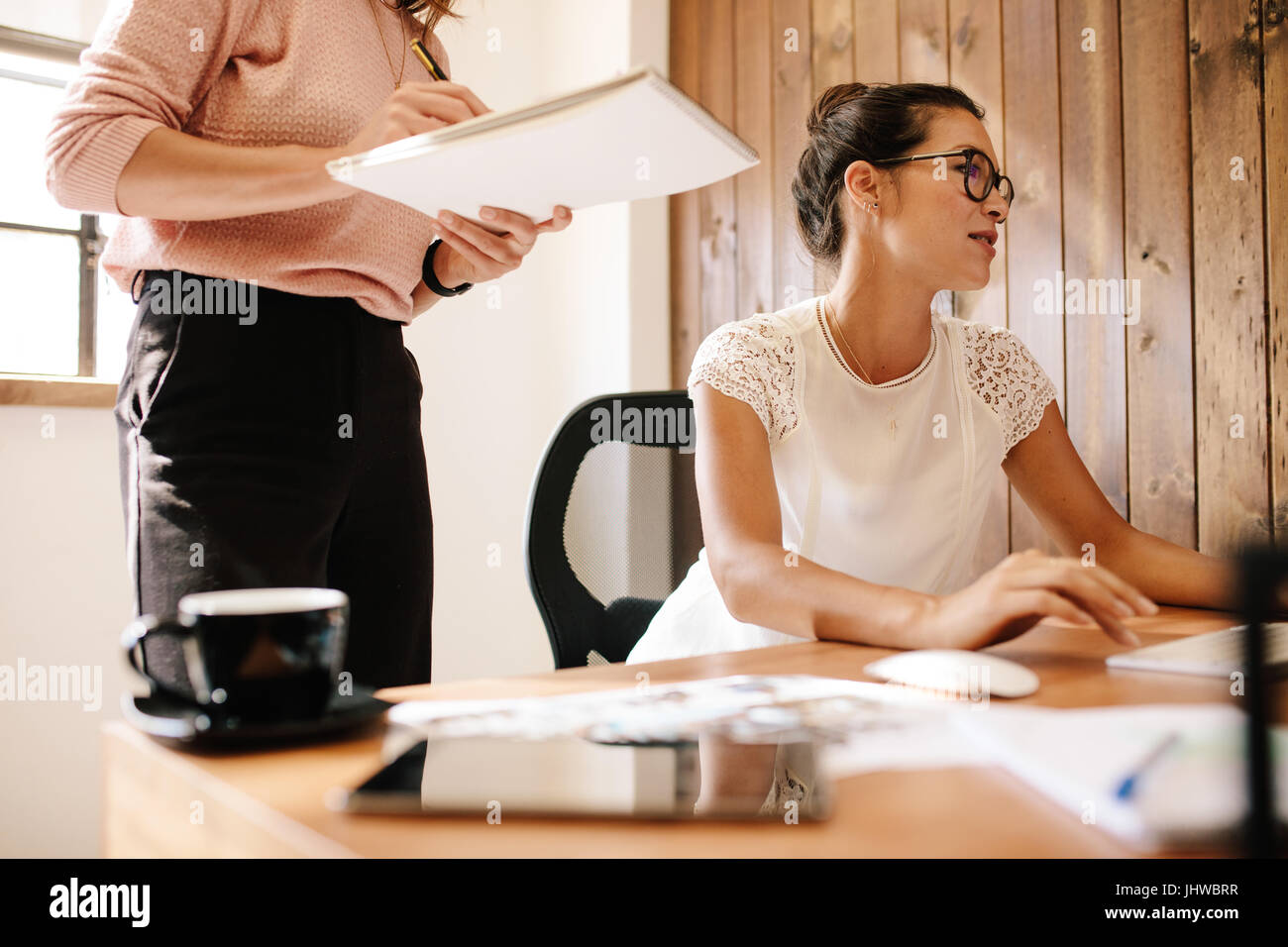 Business-Frau mit Kollegin Stand mit Notepad an ihrem Schreibtisch arbeiten. Zwei weibliche Büroangestellte bei der Arbeit. Stockfoto