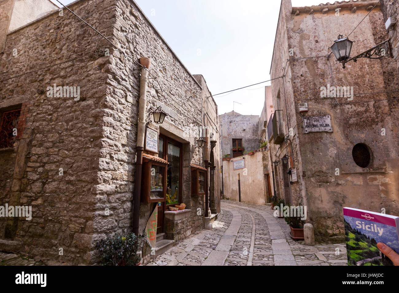 Lonely Planet Sizilien Reiseführer in einer engen Straße mit Häusern aus Stein und Kirche in Erice, Sizilien, Italien Stockfoto