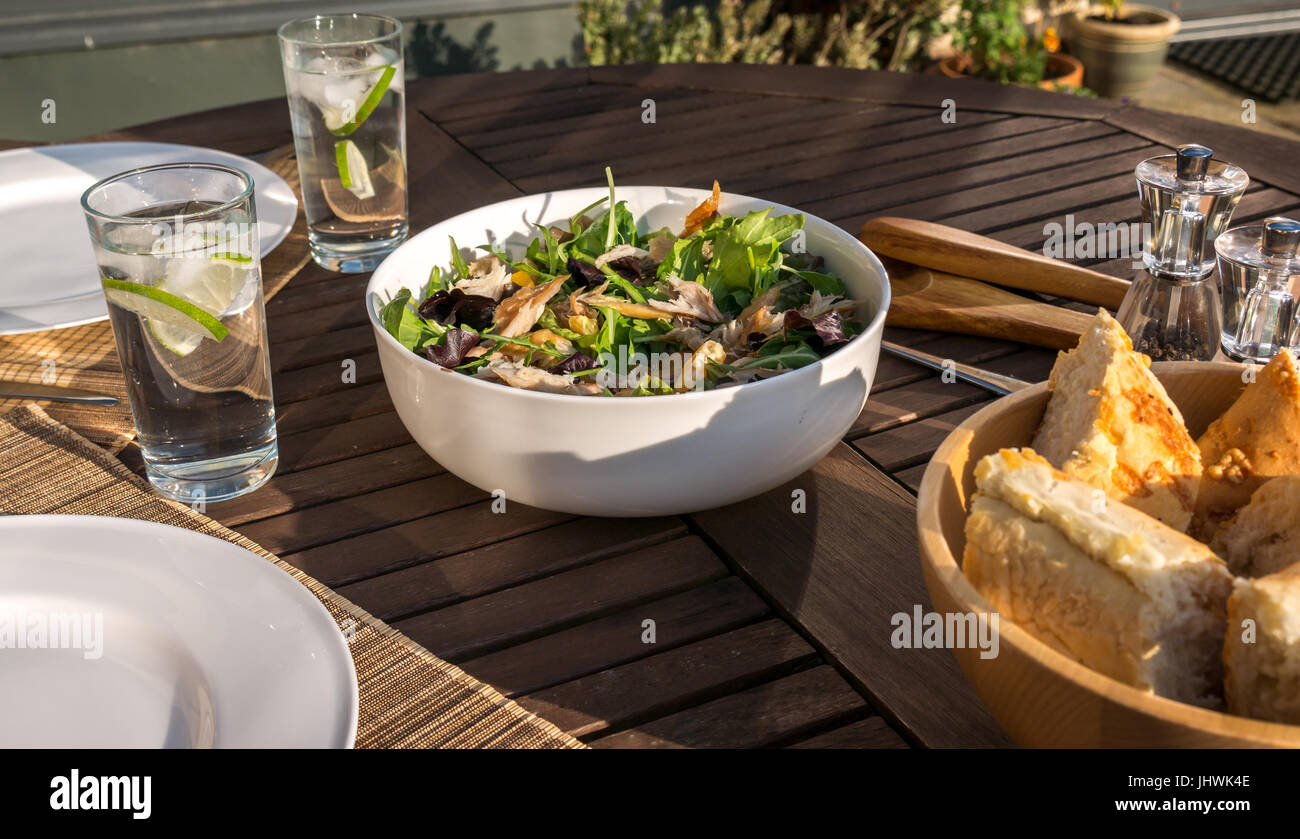 Geräucherte Makrele und Clementine Salat, serviert im Freien in weißes Geschirr Schale auf Deck Tisch mit Tellern, Gläsern, und Baguette Schüssel Stockfoto