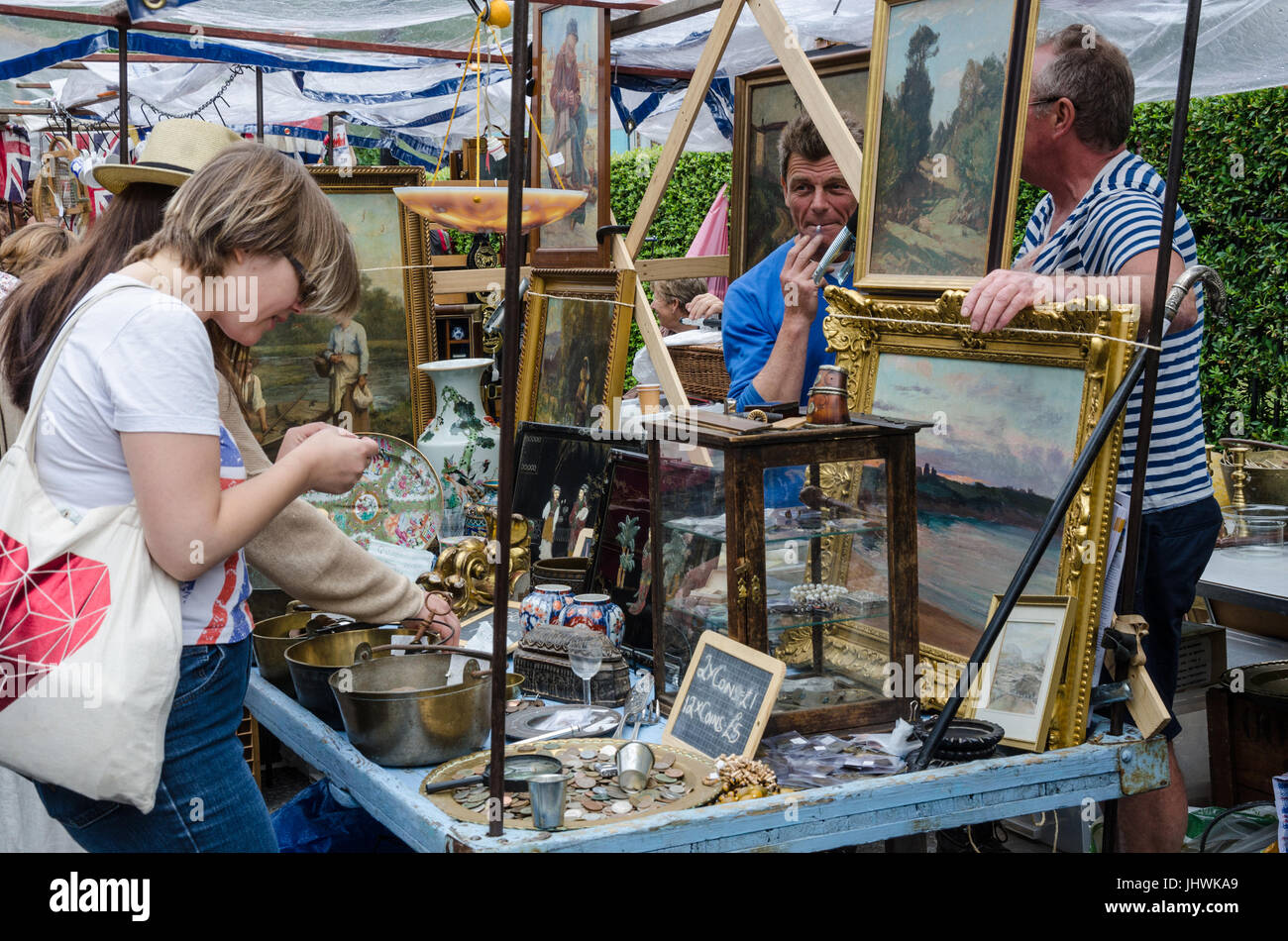 Ein paar Damen durchsuchen Elemente auf eine Antiquitäten-Stall in Portobello Road als Stall Besitzer schauen auf. Stockfoto