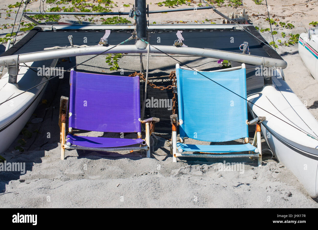 2 verwitterte Strandkörbe zwischen Katamaran Rümpfen an einem Strand in Florida Stockfoto