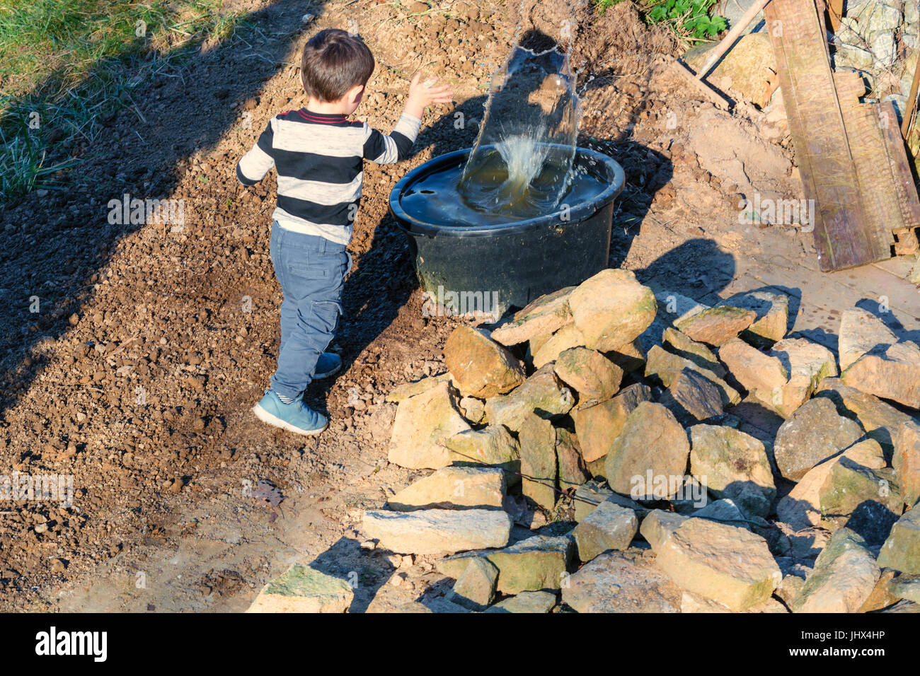 Kleiner Junge werfen einen Stein in ein Wasserfass Stockfoto