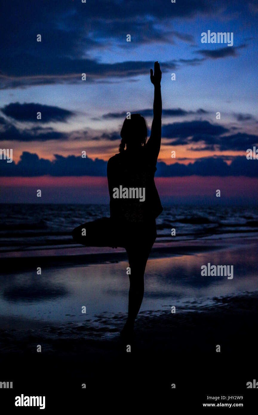 Silhouette einer Frau eine Yoga pose am Strand bei Sonnenuntergang in einem Moment der Ruhe Stockfoto