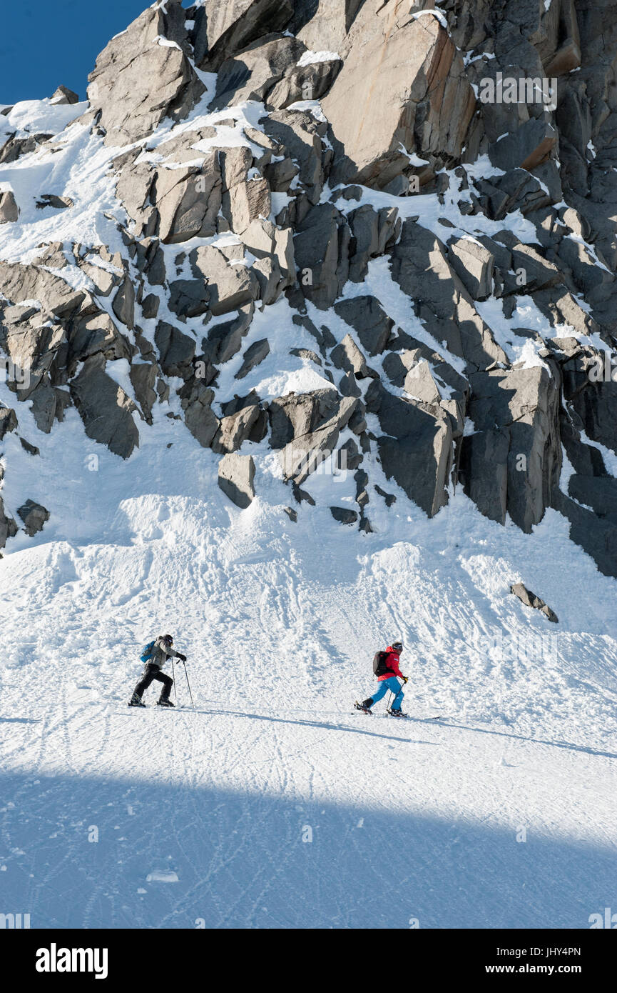 Bergführer mit Sherpa durchqueren unterhalb einer Felsformation in den Skigebieten Aerea Disentis, Schweiz Stockfoto