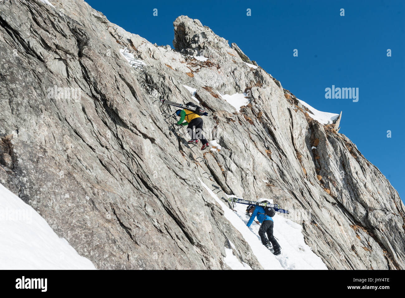 Skitour in den Bergen der Region Disentis in der Schweiz. Die Skier sind auf die Rucksäcke für den Aufstieg über eine steile Felswand montiert. Stockfoto