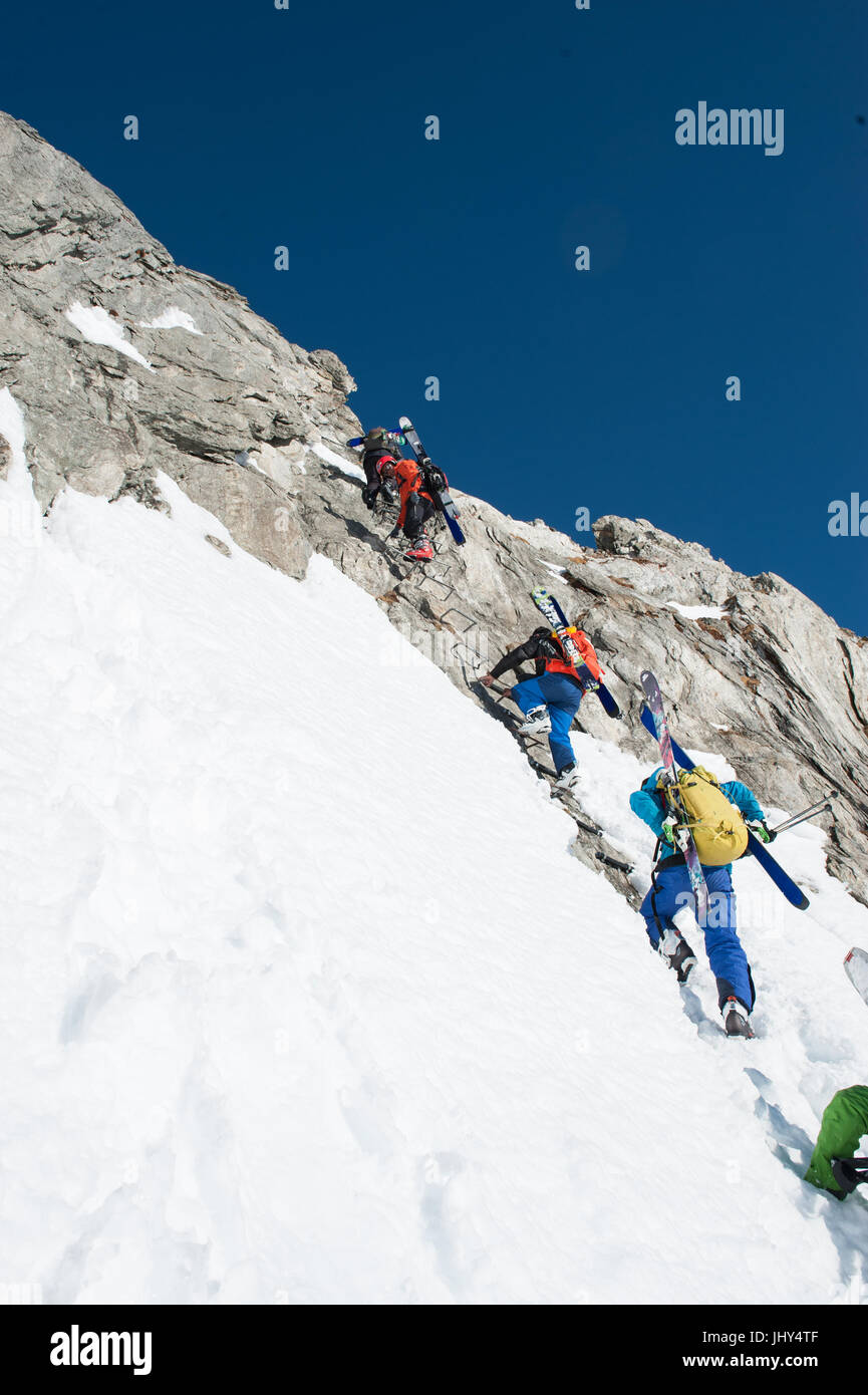 Skitour in den Bergen der Region Disentis in der Schweiz. Die Skier sind auf die Rucksäcke für den Aufstieg über eine steile Felswand montiert. Stockfoto