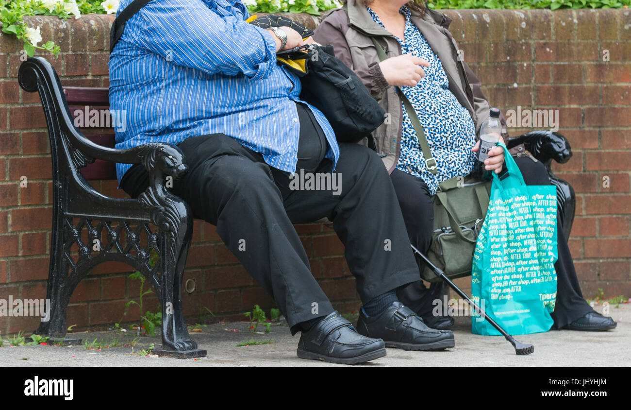 Krankhaft fettleibig. Übergewicht Paar draußen sitzen auf einer Bank in Großbritannien. Ungesunde Lebensweise. Die übergewichtigkeit. Stockfoto
