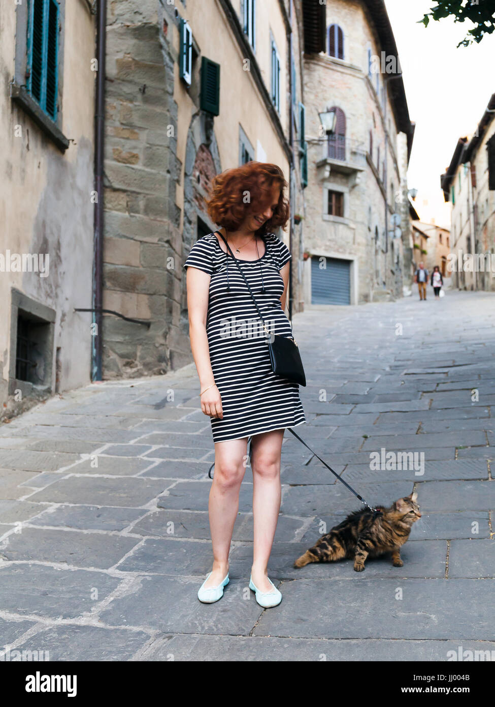 Cortona, Italien - 15. Juli 2017: Mädchen flaniert durch die Straßen der kleinen toskanischen Stadt mit ihrer Katze an der Leine. Stockfoto