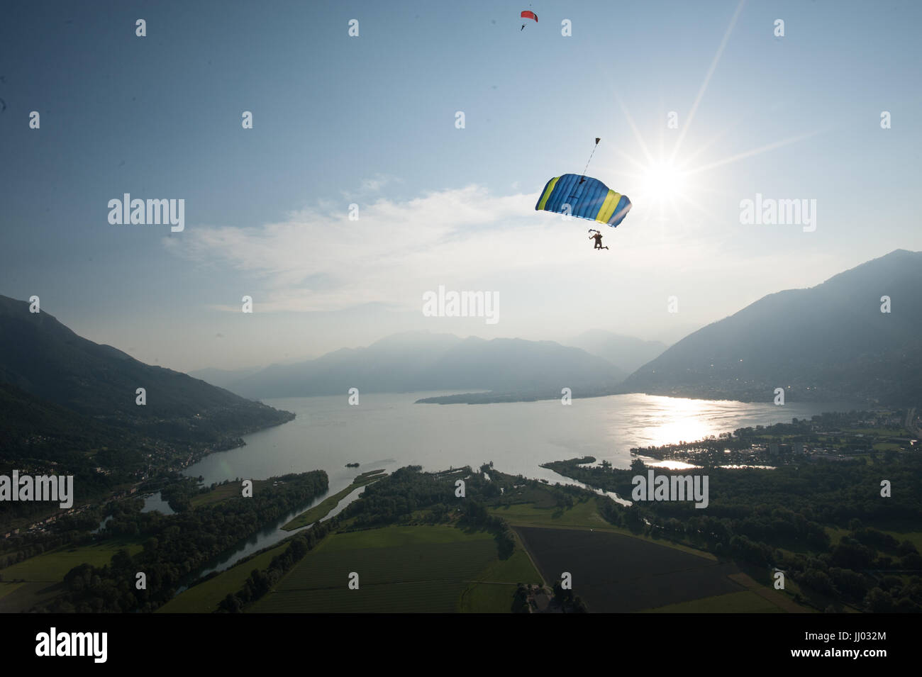 Fallschirmspringer drehen nach unten mit ihren Parachtue mit Lago Maggiore im Hintergrund und die Sonne niedrig über die Berge Stockfoto