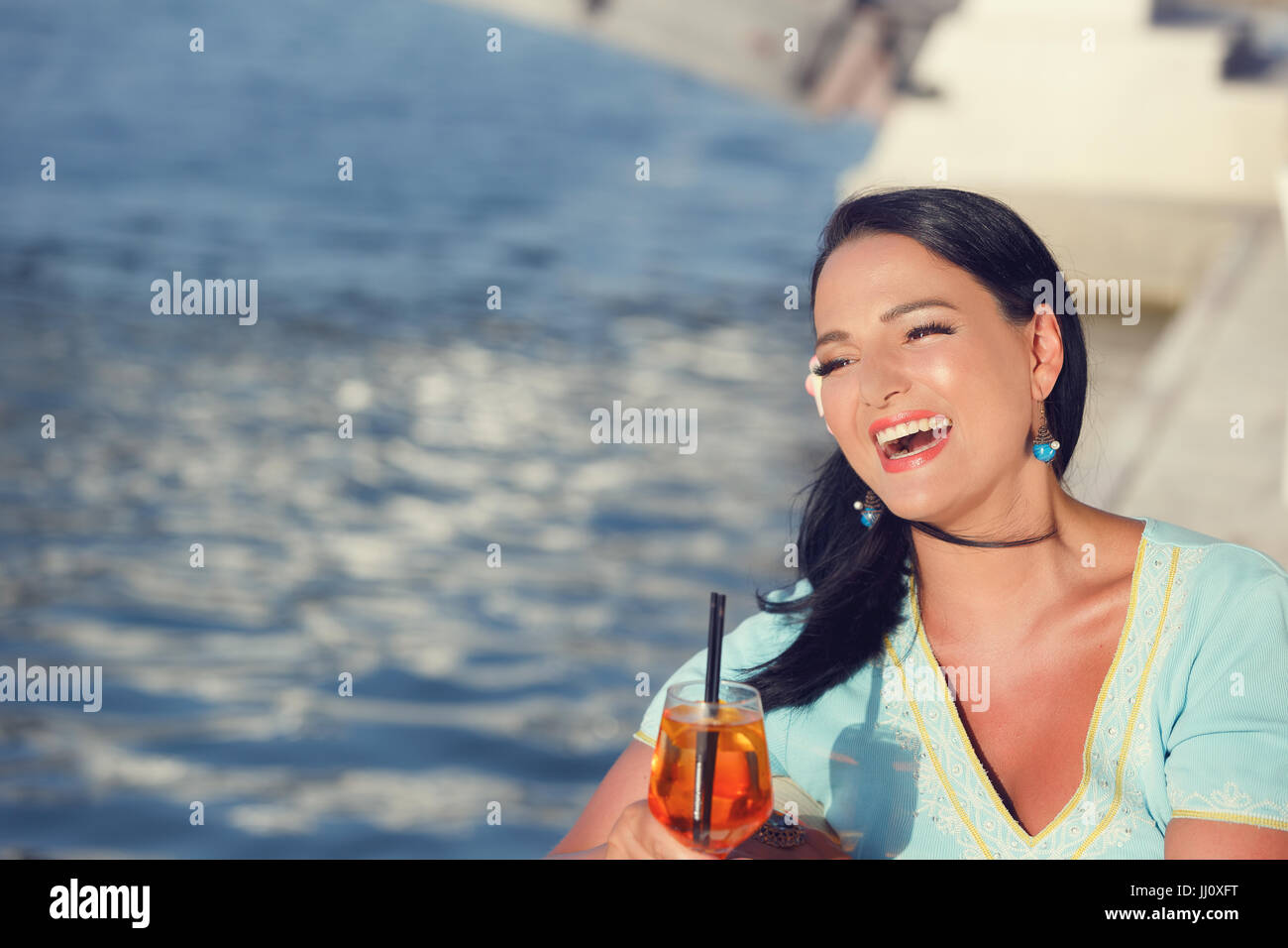 Wunderschöne lächelnde Frau sitzen im Café am Meer trinken cocktail und auf der Suche zur Seite. Ihr Haar vom Wind. Textfreiraum auf der linken Seite Stockfoto