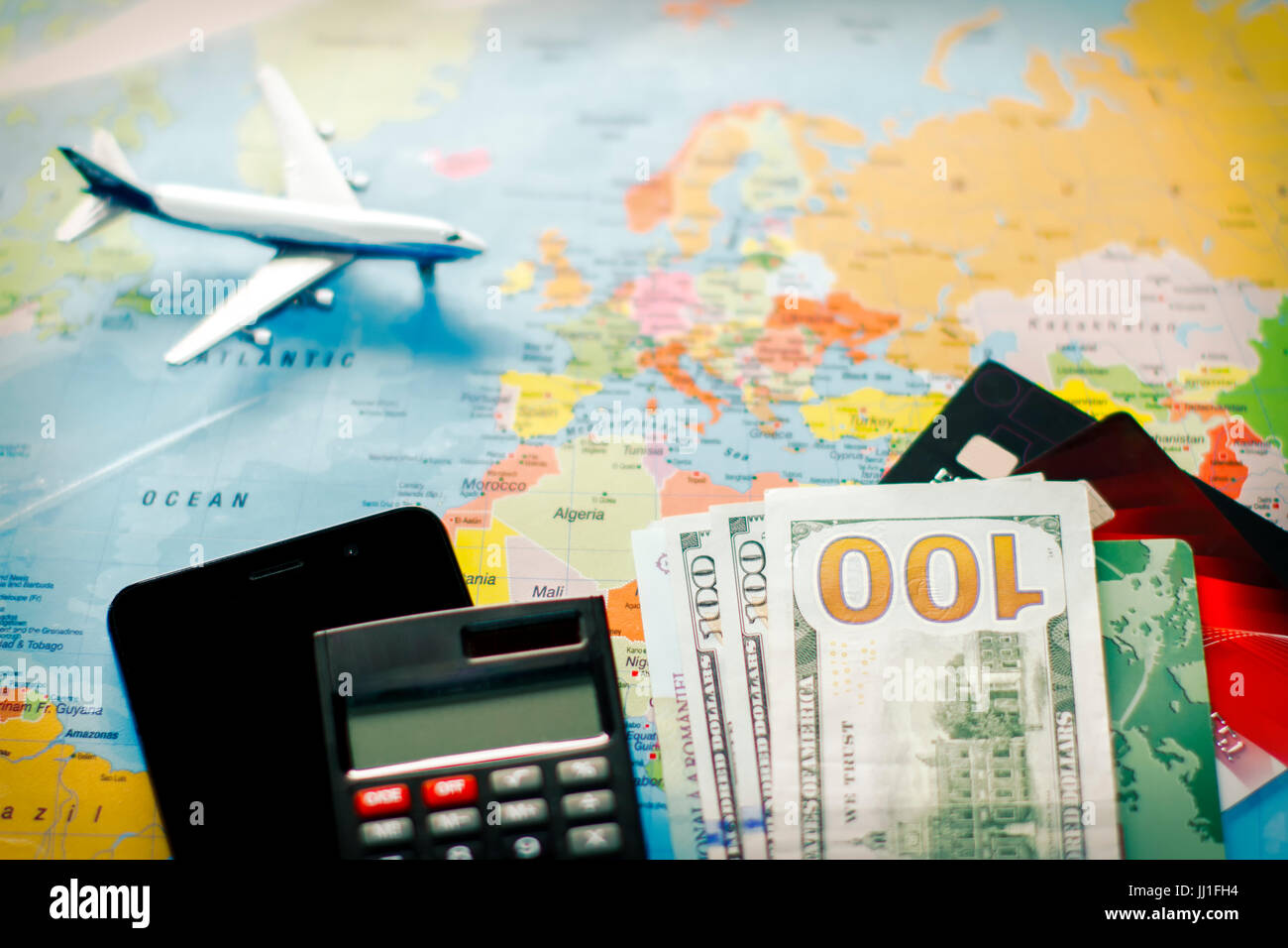 Reiseplanung mit US-Dollar-Banknoten, Taschenrechner, Smartphone und Flugzeug auf Weltkarte – Finanz-, Budget- und Tourismuskonzept. Stockfoto