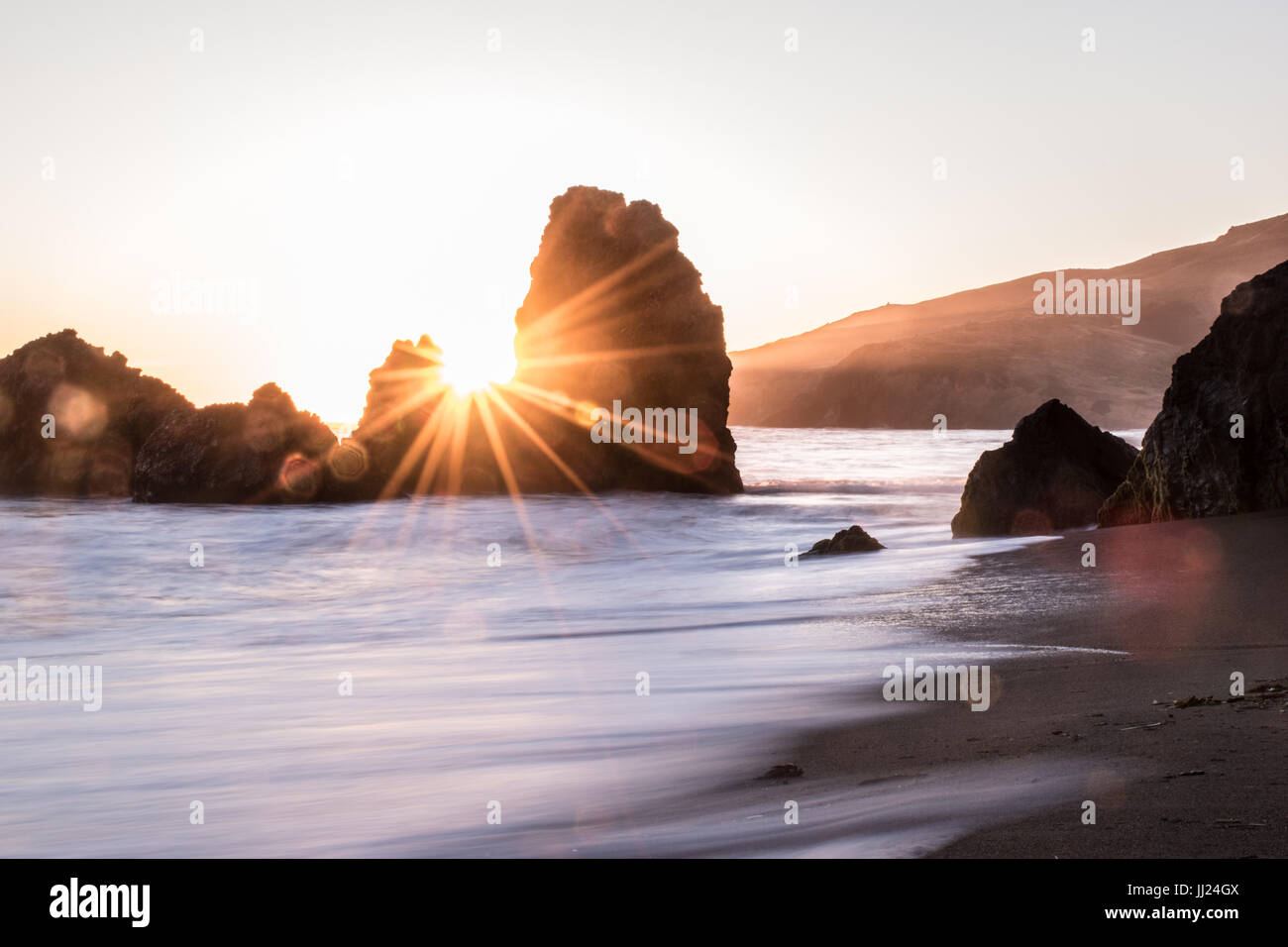 Sonnenuntergang an der Golden Gate mit goldenen Strahlen teilen zwei Felsen am Strand mit Sand und Wellen Stockfoto