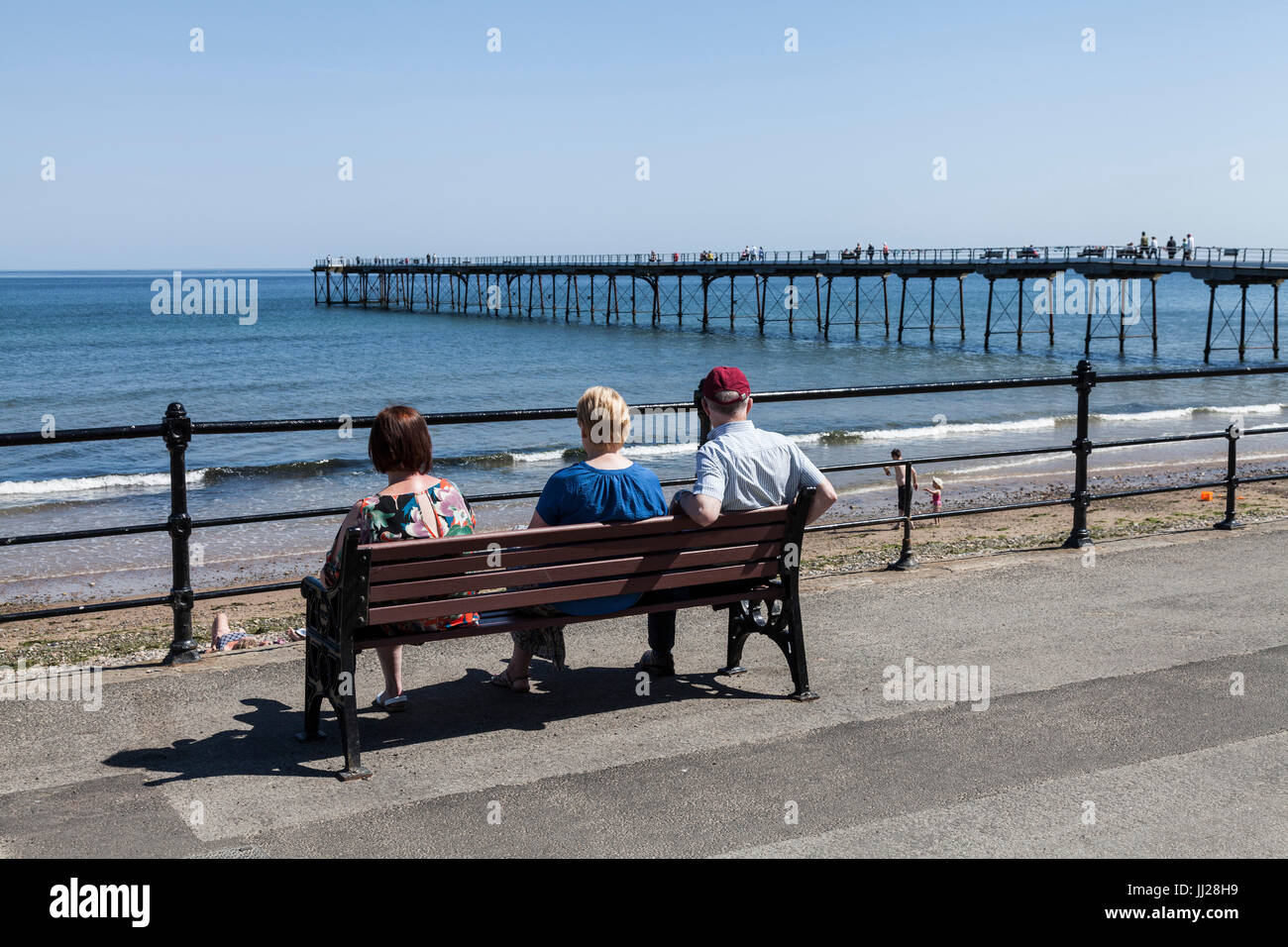 Drei Leute saßen auf einer Bank, Blick auf das Meer bei Saltburn am Meer, England, UK Stockfoto