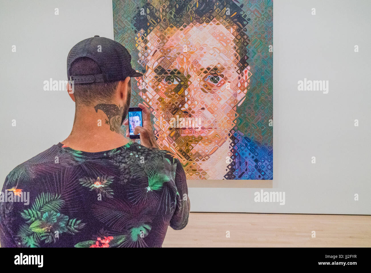 Junge männliche Erwachsene nutzt mit einem Hals Tattoo sein Handy, um ein großes Gemälde des Künstlers Chuck Close in einem Kunstmuseum zu fotografieren. Das Bild der th Stockfoto