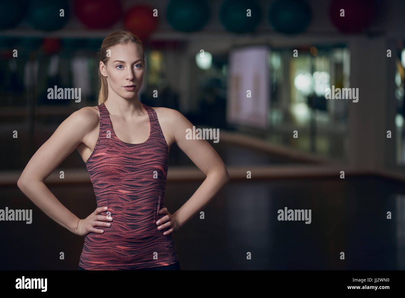 Drei Viertel Hände auf den Hüften Körper Porträt der sportliche junge Frau posiert in Fitness-Studio mit Stockfoto
