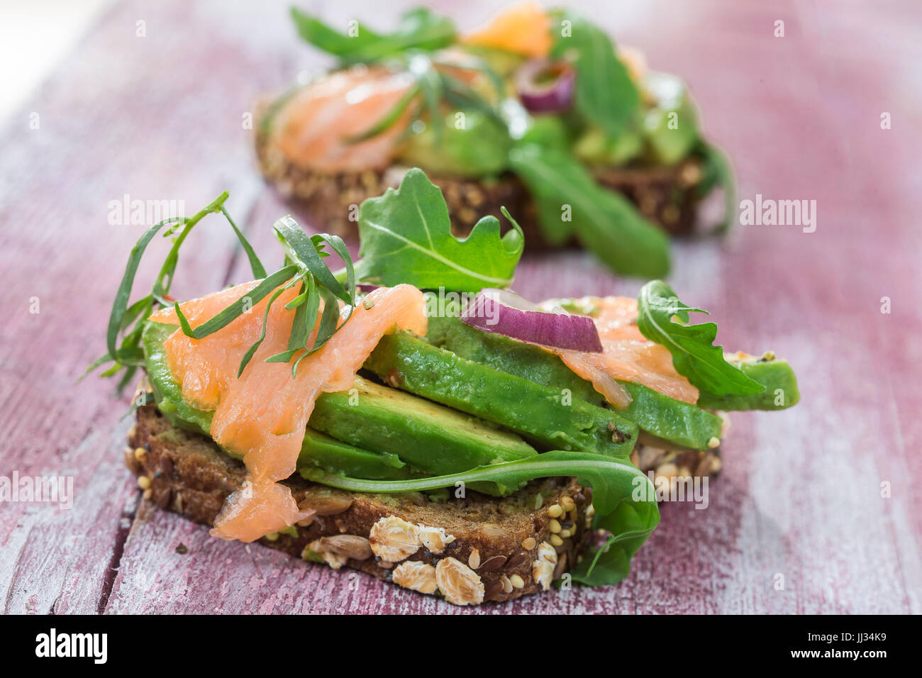 Countrybread Avocado, gesalzener Lachs Sandwich mit frischen Kräutern auf rosa craked Paintt Holzbrett Hintergrund. Gesunde Ernährung-Thema Stockfoto