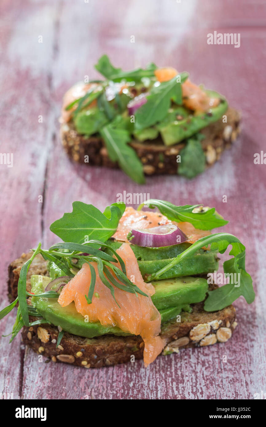 Countrybread Avocado, gesalzener Lachs Sandwich mit frischen Kräutern auf rosa craked Paintt Holzbrett Hintergrund. Gesunde Ernährung-Thema Stockfoto