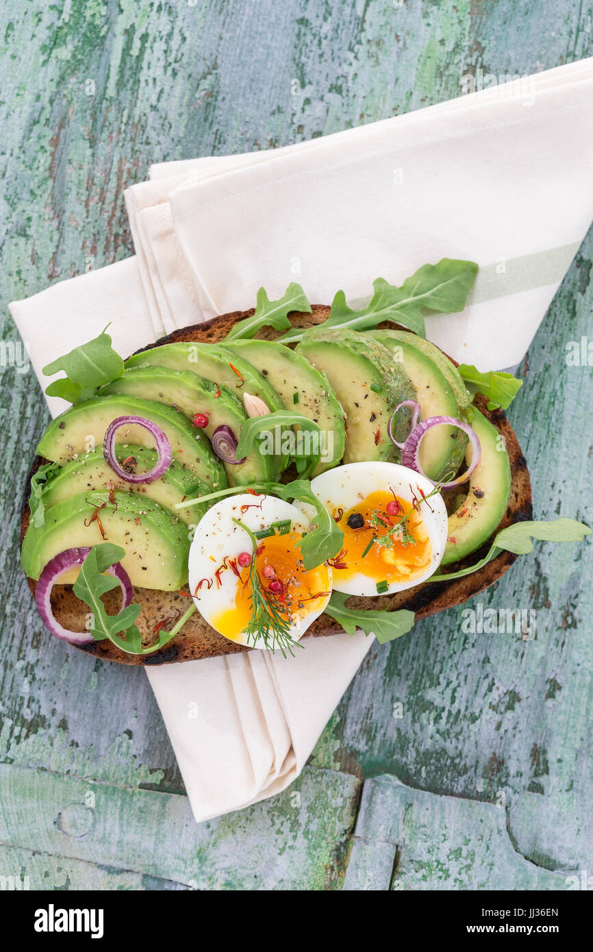 Vollkornbrot Avocado, pochiertem Ei-Sandwich mit frischen Kräutern, roten Zwiebeln auf Geschirrtuch Holzbrett Hintergrund. Gesunde Ernährung-Thema Stockfoto