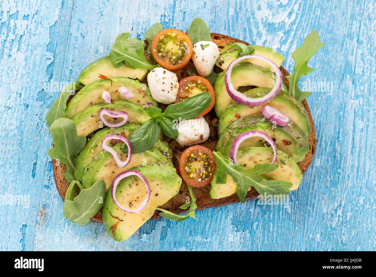 Vollkornbrot Avocado, Tomaten, Mozzarrela Sandwich mit frischen Kräutern, roten Zwiebeln auf Geschirrtuch Holzbrett Hintergrund. Gesunde Ernährung-Thema Stockfoto