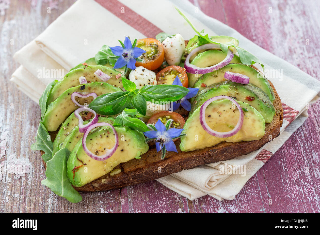 Vollkornbrot, Avocado, Smok Lachs Sandwich mit frischen Kräutern, roten Zwiebeln auf Geschirrtuch Holzbrett Hintergrund. Gesunde Ernährung-Thema Stockfoto