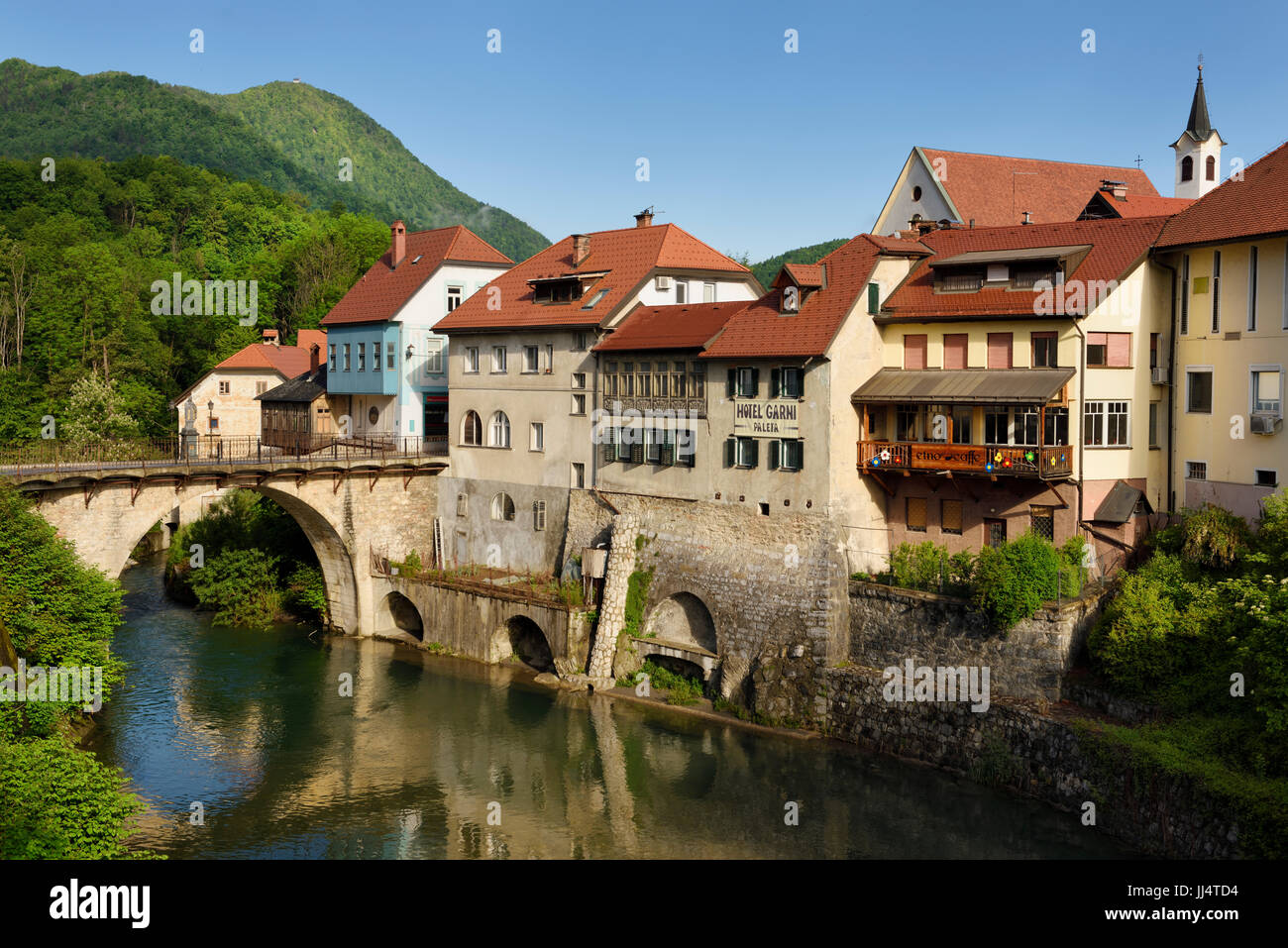 Älteste Steinbrücke in Slowenien Kapuziner Brücke und Kirche Glockenturm am Fluss Selca Sora mit steinernen Mauern umgebene Flussufern in Skofja Loka Dorf Stockfoto